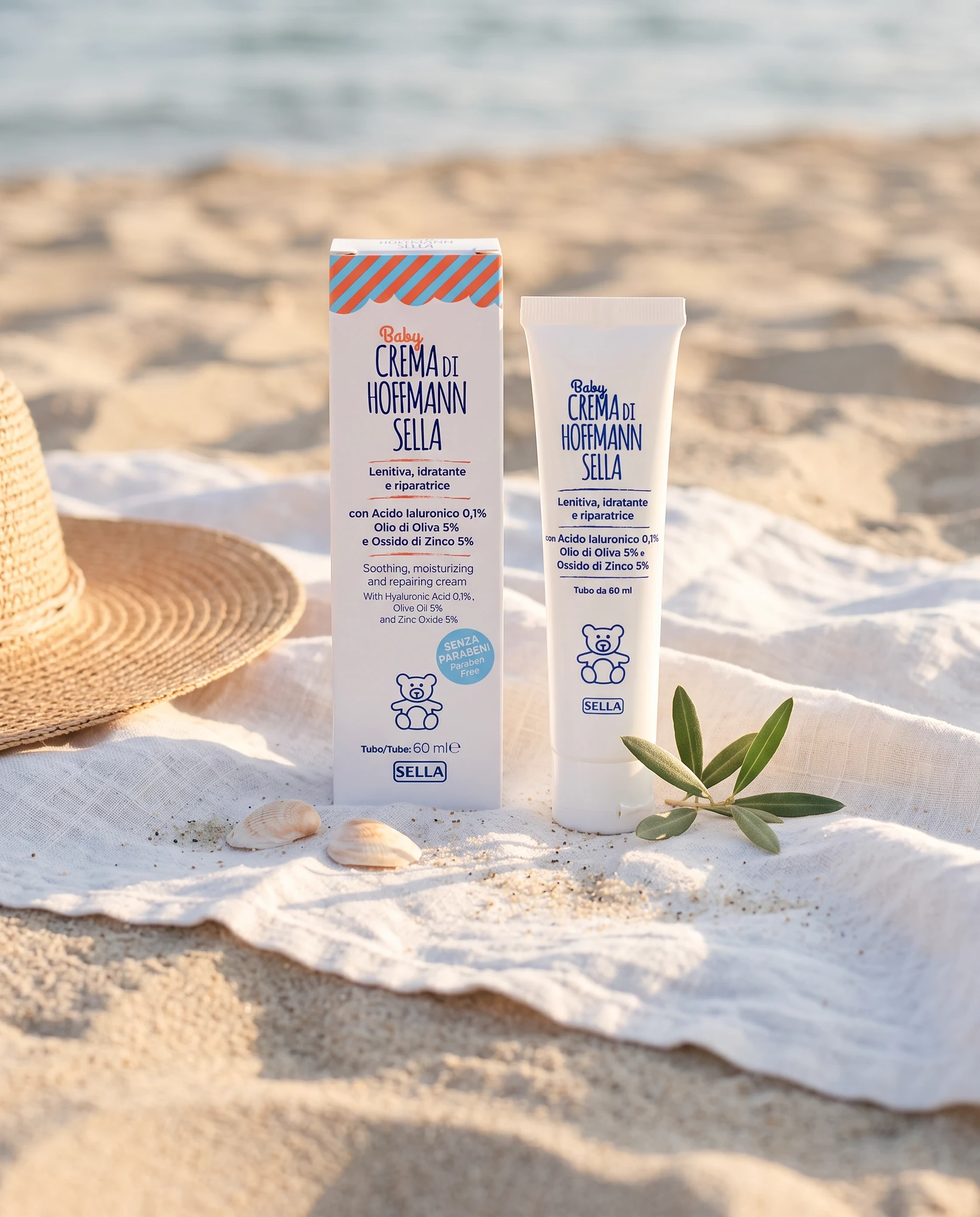 Tube and pack of Baby Crema di Hoffmann Sella on a beach towel with a straw hat and seashells