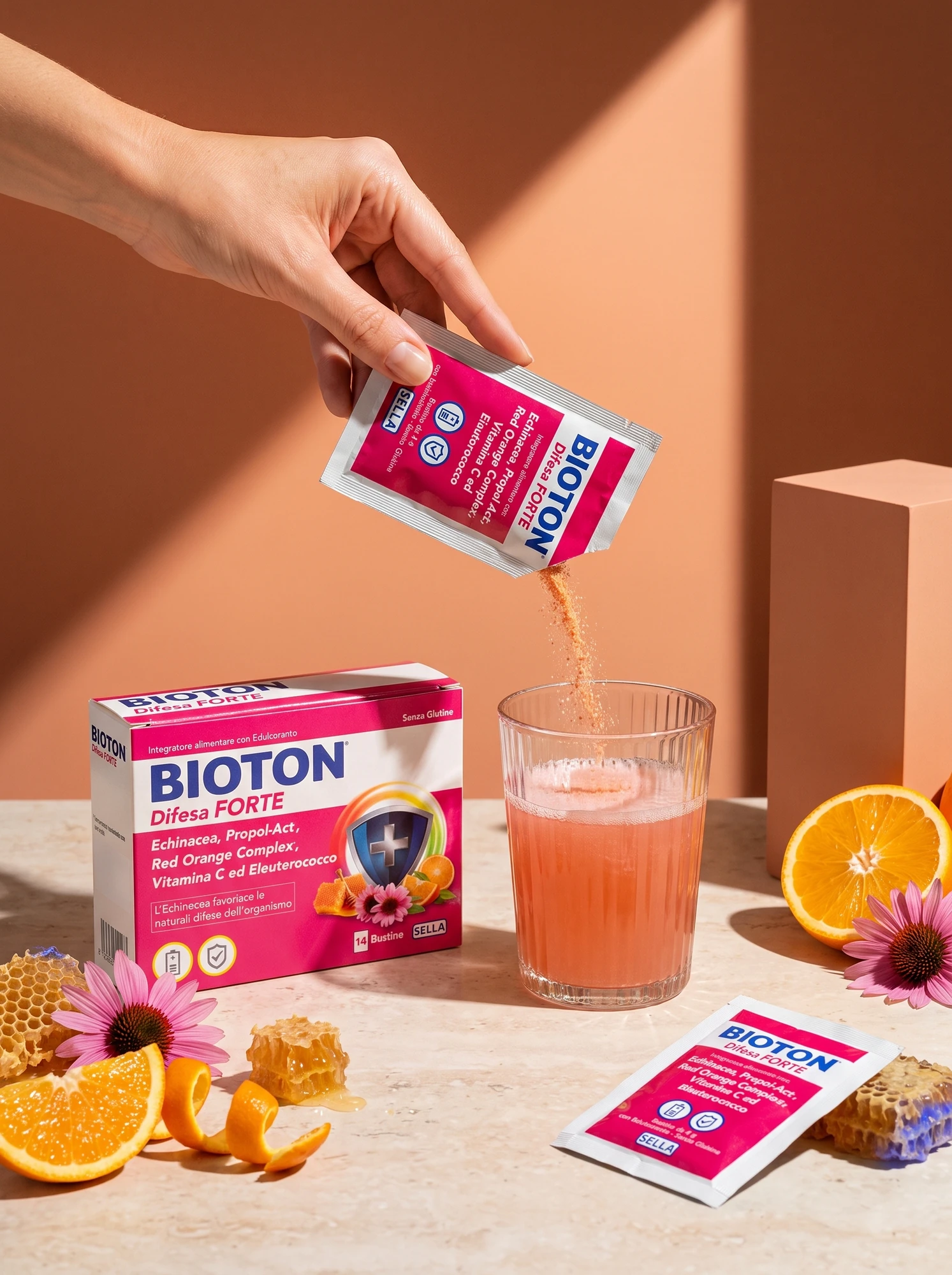 Hand pouring a sachet of Bioton Difesa Forte into a glass beside the pack and oranges