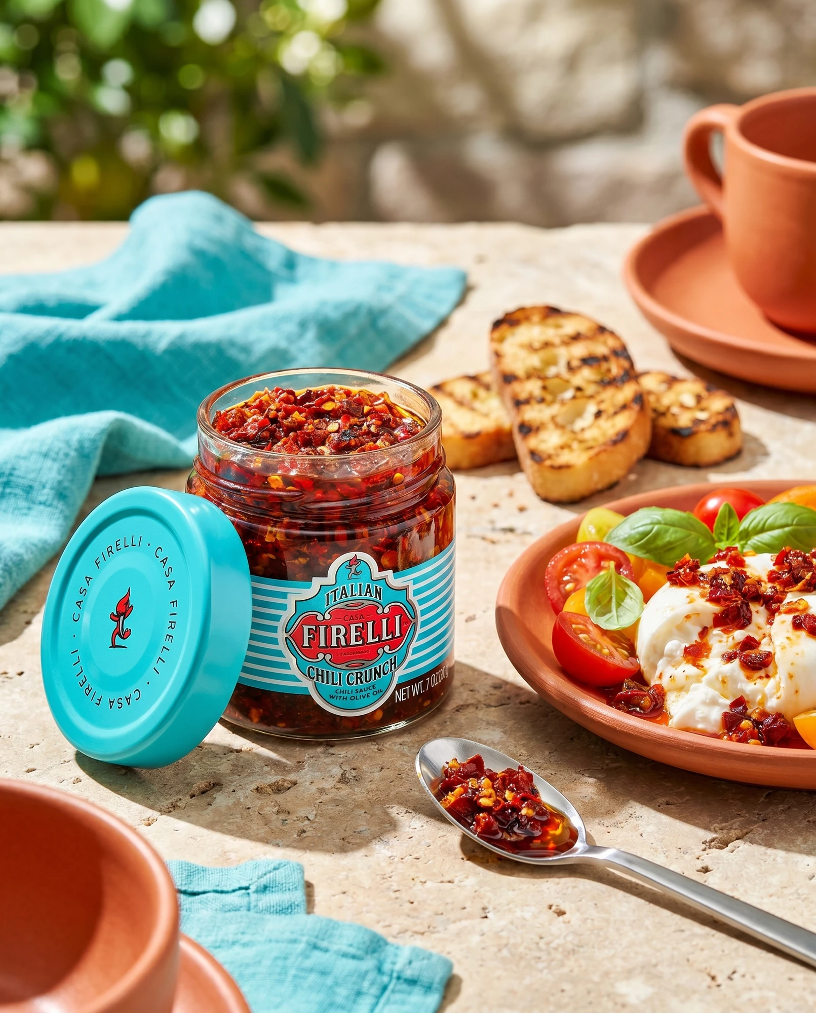 Jar of Casa Firelli Chili Crunch beside bruschetta and burrata topped with chilli crunch