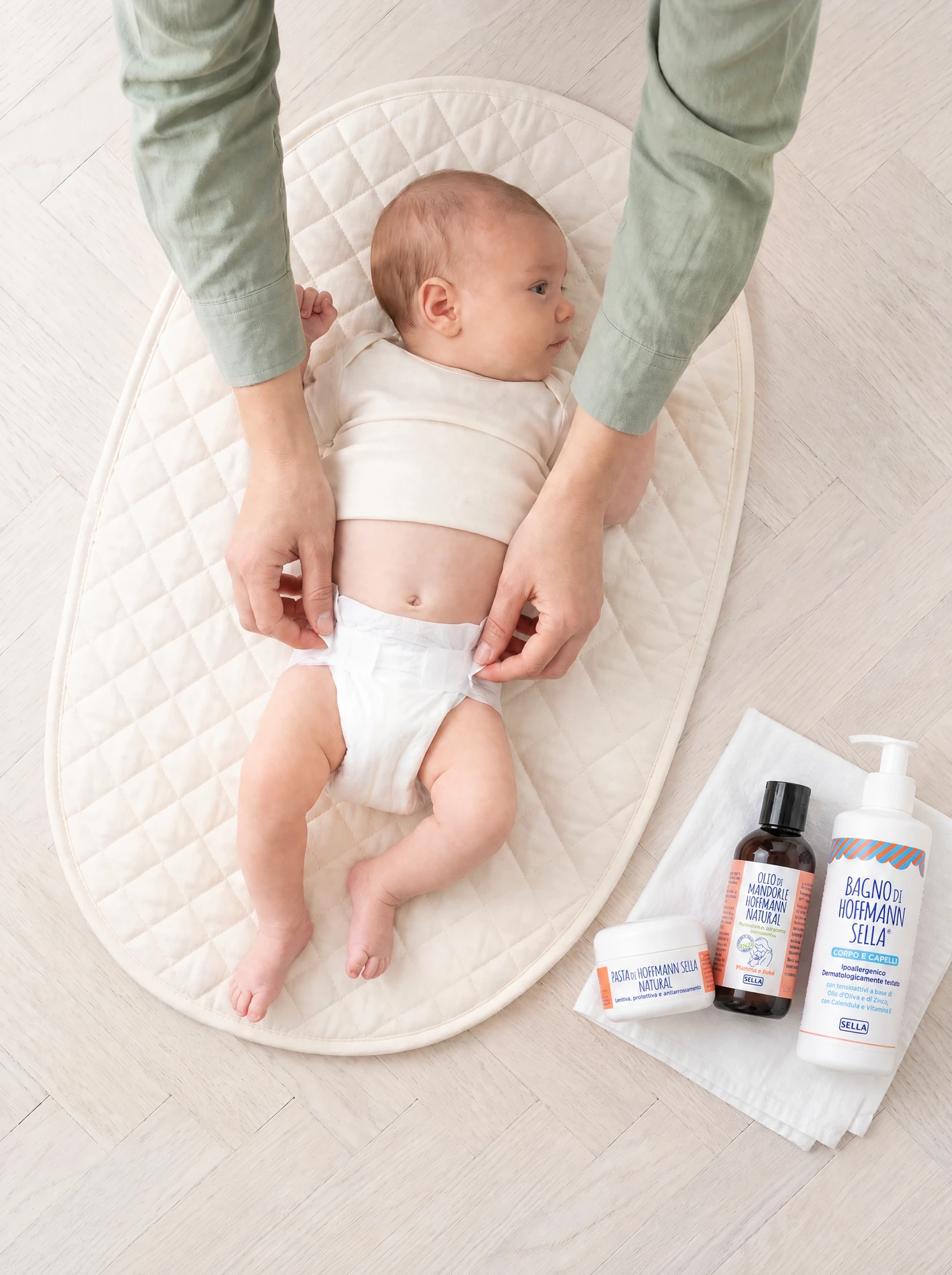 Newborn baby on a changing mat during a nappy change, with Pasta, Olio di mandorle and Bagno di Hoffmann Sella