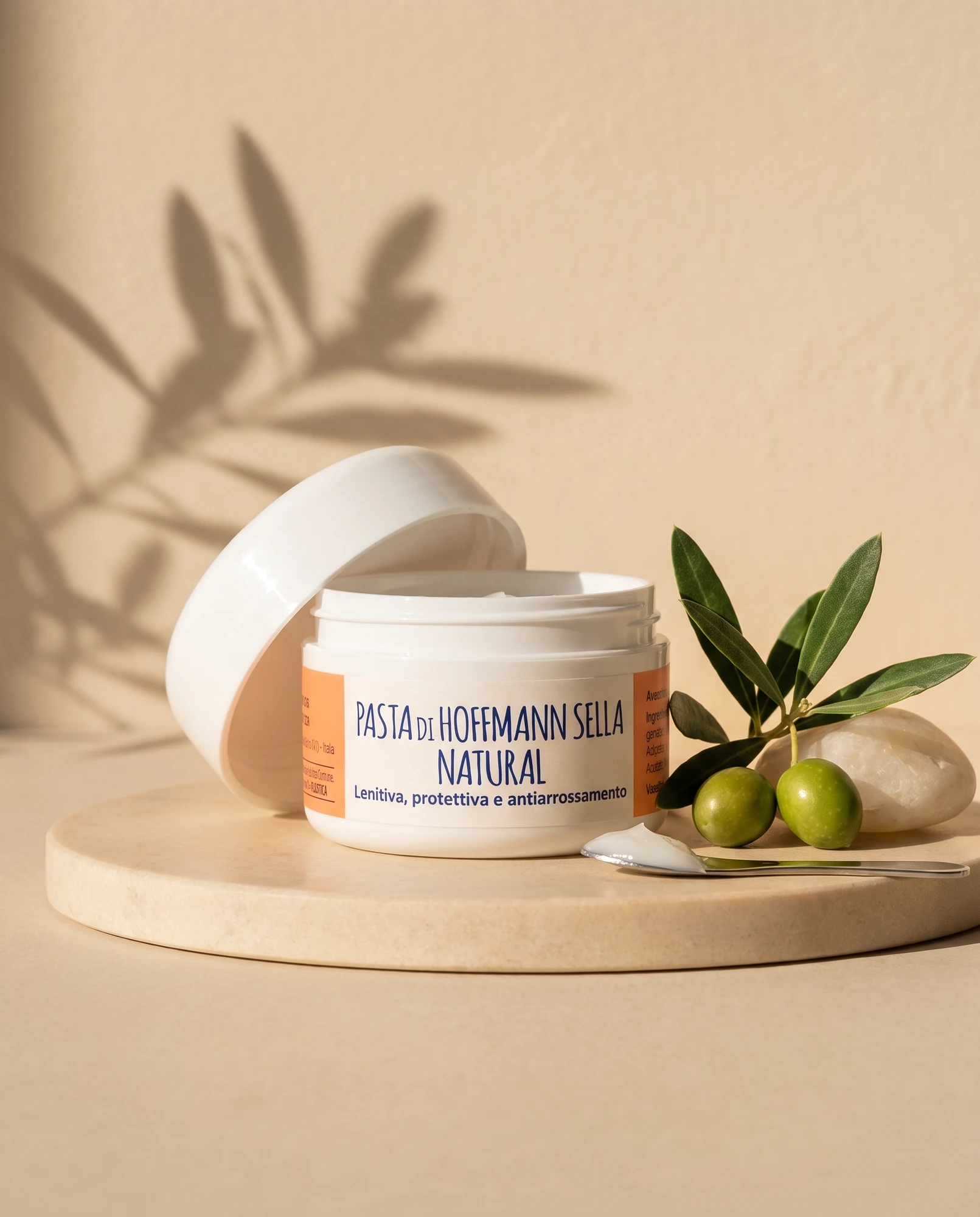 Open jar of Pasta di Hoffmann Sella Natural on a marble tray with an olive sprig and olives