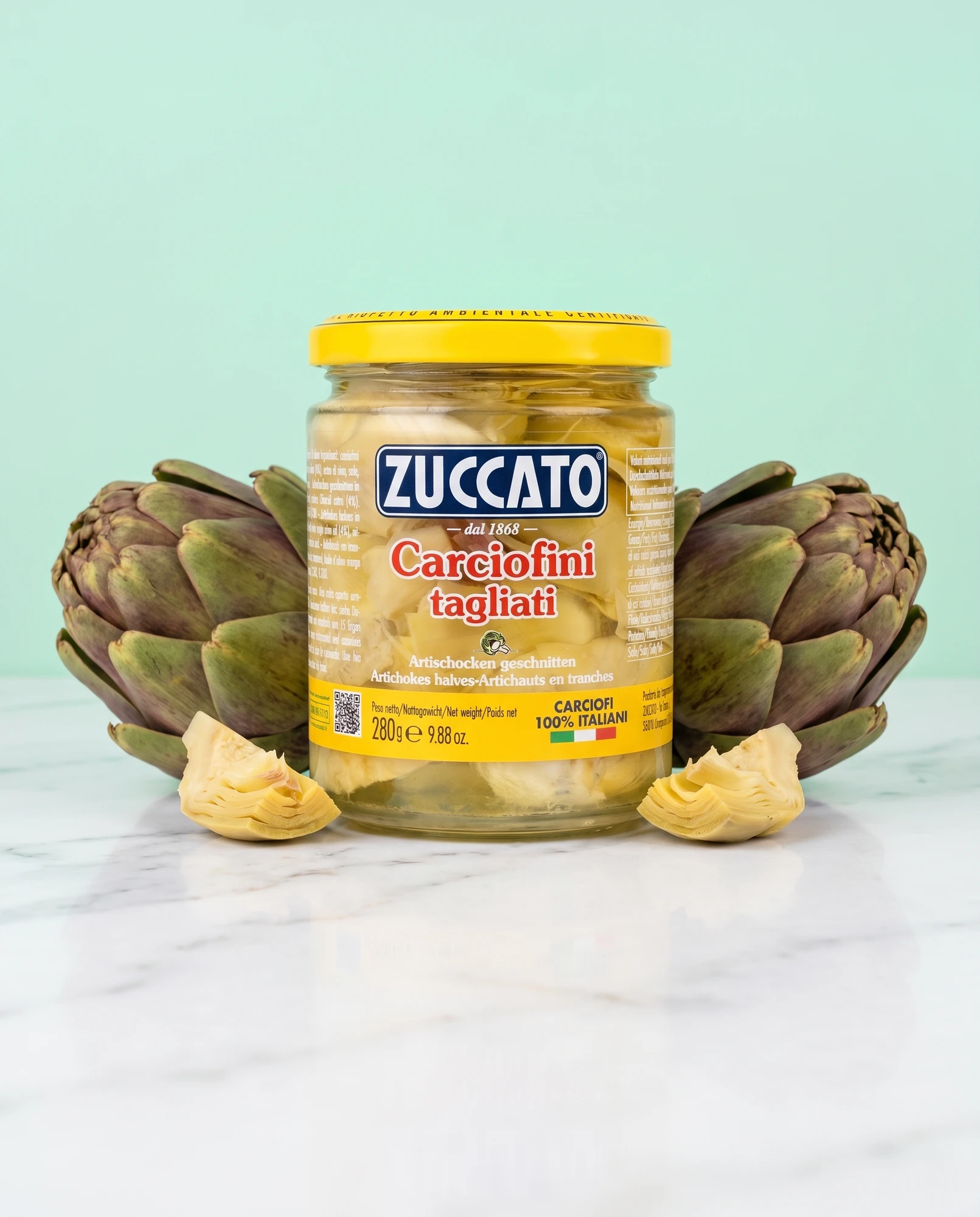 Jar of Zuccato Carciofini tagliati between two whole artichokes against an aqua background