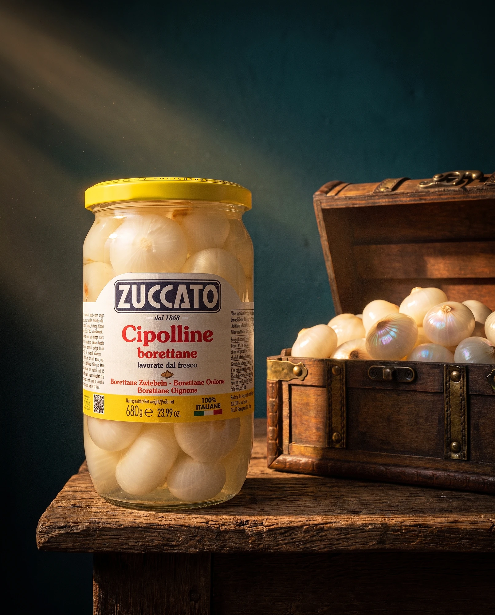 Jar of Zuccato Cipolline borettane beside a wooden chest filled with small onions