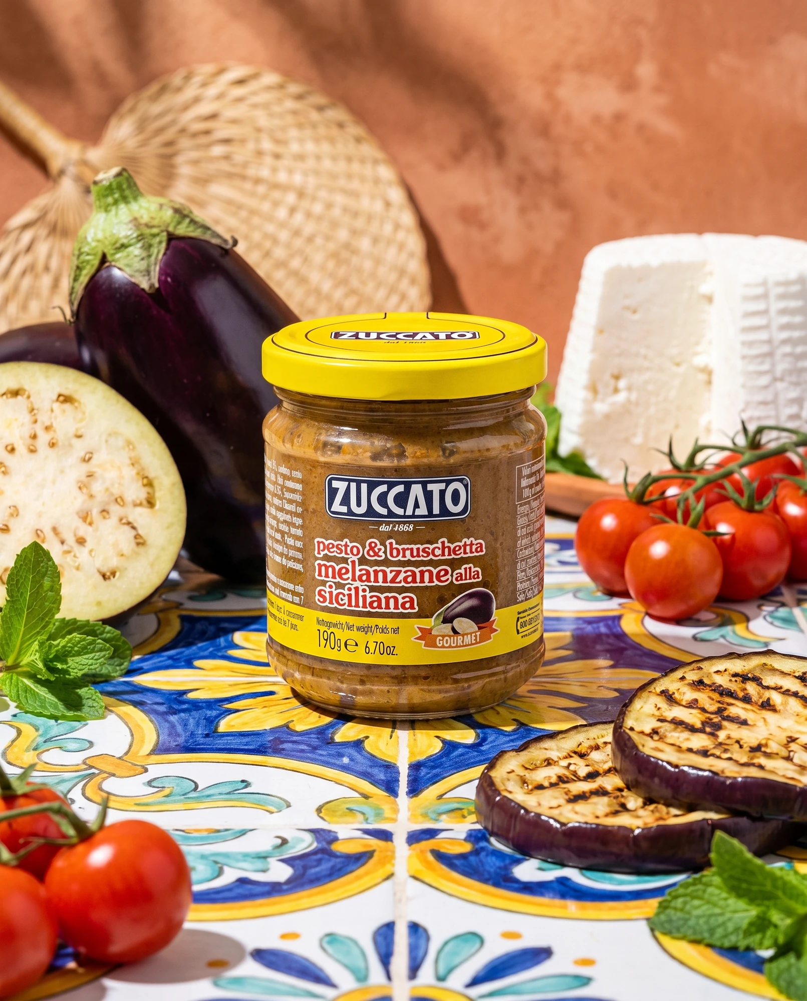 Jar of Zuccato Pesto e bruschetta di melanzane alla siciliana on majolica tiles with aubergines, ricotta and cherry tomatoes